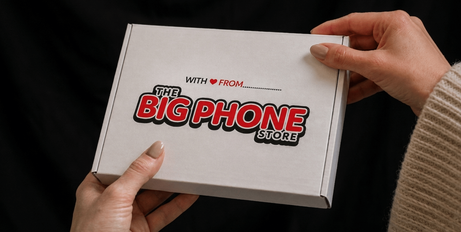 a woman with a knitted jumper holding The Big Phone Store packaging with a dark background